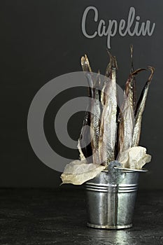 Capelin cold smoked fish in a decorative bucket on a dark background.