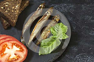 Capelin cold smoked fish on a round slate plate on a black-gray