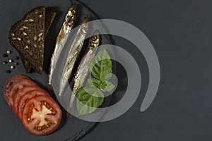 Capelin fish of cold smoked on round slate plate on black background.