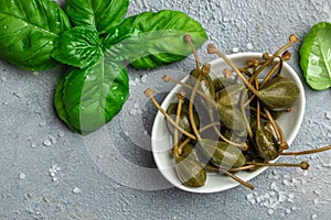 Capers. Marinated or pickled canned capers fruit with fresh rosemary in a small bowl, on gray background. place for text, top view