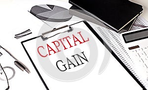 CAPITAL GAIN text on paper clipboard with chart and notebook on withe background