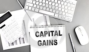 CAPITAL GAINS text written on notebook on grey background with chart and keyboard, business concept