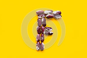 Capital letter F from dry uncooked red and white speckled beans legumes on bright yellow background. Creative food typography art