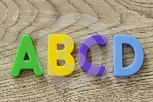 Capital letters A B C D in flat colorful plastic letter toys on gray wooden background