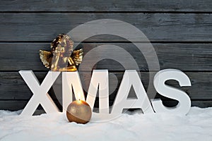 Capital letters forming the word xmas golden putto figurine and candle on pile of snow against wooden wall