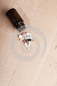 Caplets or pills in the opening of a medicine bottle on wooden board, view from above