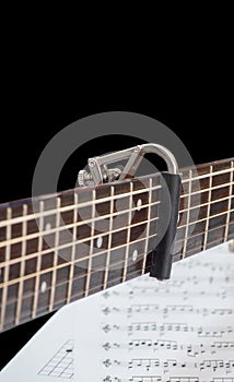 Capo on the Acoustic guitar neck , score note blackground under the capro and guitar. capro made from aluminium, Selective focus