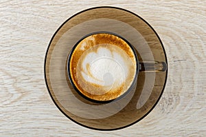 Cappuccino in brown cup in saucer on wooden table. Top view