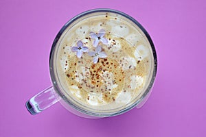 Cappuccino with cinnamon on a pink background. Lilac flowers in coffee foam