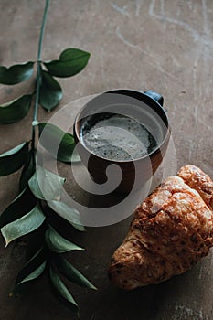 Cappuccino coffee and croissant on wooden background on the table. Perfect breakfast in the morning. Rustic candid style