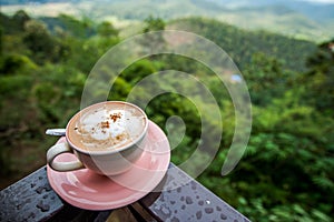 Cappuccino Coffee in a cup with leaf art foam on top with mountain landscape view behind