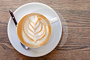 Cappuccino coffee dressing with leave shape of latte art on wood table,