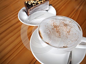 Cappuccino coffee in white cup with chocolate crepe cake on wood
