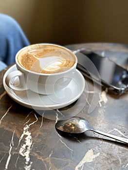 Cappuccino coffee in white cup on marble table with spoon.