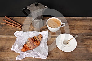 Cappuccino coffee in a white cup and saucer and chocolate muffin in paper on an old wooden table, coffee maker, food enjoyment