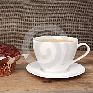 Cappuccino coffee in a white cup and saucer and chocolate muffin in paper on an old wooden table, dark background, concept of