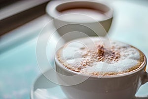 Cappuccino coffee on wooden table and sunlight background