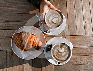 Cappuccino and croissant on the table in the cafe. Delicious breakfast. Womens hands hold a cup of Cappuccino