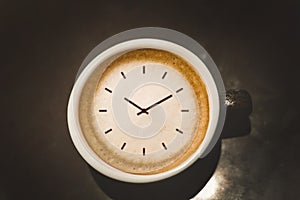 Cappuccino cup with clock face standing on black table close up