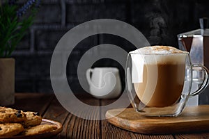 cappuccino in cup and geyser coffee maker on wooden table with black brick wall as background