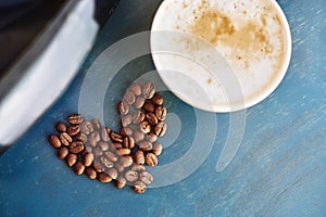 A cappuccino Cup with a heart shape made of coffee beans on a blue wooden table