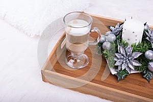 A cappuccino drink and Christmas decoration with candle, fir branch and silver balls on white furry carpet