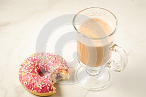 Cappuccino glass with bitten donut/cappuccino glass with bitten donut on a white marble background. Top view