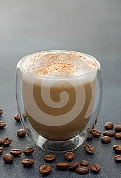 cappuccino in glass cup and coffee beans on grey table