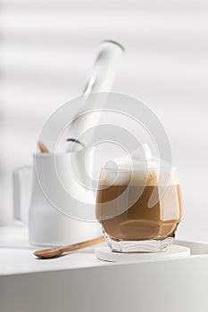 Cappuccino in a glass cup on a white wooden table.