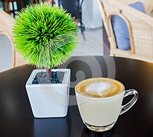Cappuccino or latte coffee with green tree on table wooden
