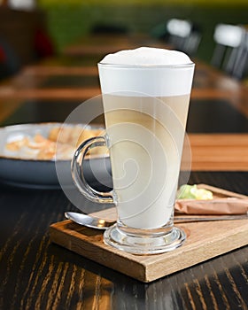 Cappuccino or latte coffee in a tall glass served in restaurant or cafe on wooden table