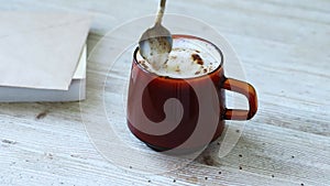 Cappuccino, latte with froth milk in cup. Spoon scoops whipped cream from glass of coffee.