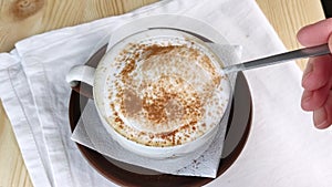 Cappuccino or latte. Spoon scoops milk froth from cup of coffee. Foam is sprinkled with cinnamon and cocoa powder. Making creamy