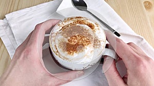 Cappuccino or latte. Two hands hold cup with milk froth, sprinkled with cinnamon and cocoa powder. Drink with creamy foam. Close-