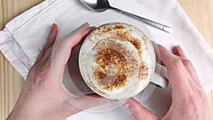Cappuccino or latte. Two hands hold cup with milk froth, sprinkled with cinnamon and cocoa powder. Drink with creamy foam. Close-
