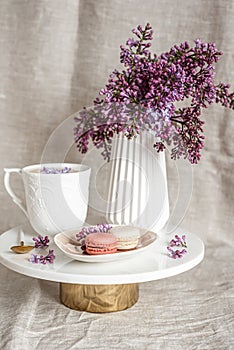 Cappuccino with macaroons on linen tablecloth, violet lilac flowers