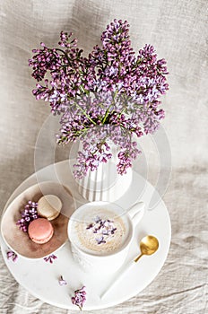 Cappuccino with macaroons on linen tablecloth, violet lilac flowers