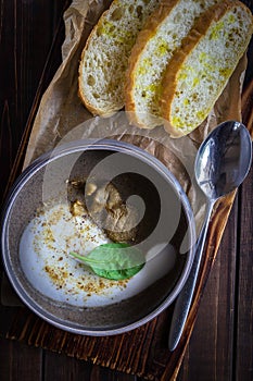 Cappuccino soup with boletus on wooden cutting board. Three slices of white bread and a spoon on the brown wooden background in