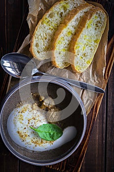 Cappuccino soup with mushrooms on wooden cutting board. Three slices of white bread and a spoon on the brown wooden background in