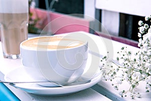 Cappuccino in a white ceramic cup and saucer on a white wooden bench