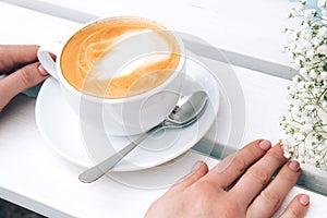 Cappuccino in a white ceramic cup and saucer on a white wooden bench