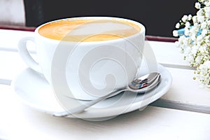 Cappuccino in a white ceramic cup and saucer on a white wooden bench