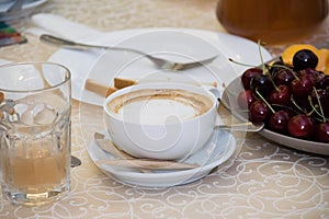 Cappuccino in a white cup with sugar in sticks on the table during breakfast