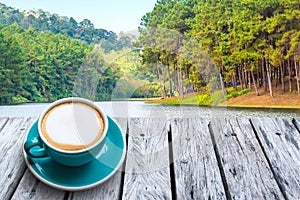 Cappuccino on a wooden table and Green forest landscape.