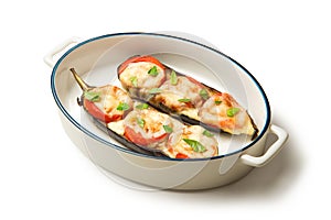 Caprese of baked eggplant tomatoes and mozzarella in an oval baking dish isolated on a white background.