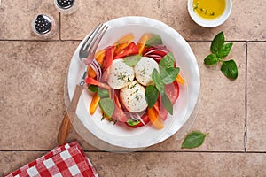 Caprese salad. Italian caprese salad with sliced tomatoes, mozzarella cheese, basil, olive oil in white plate over old brick tiles