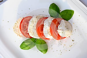 Caprese salad made with fresh soft white italian cheese mozzarella buffalo, green basil, red tomatoes and origano herb photo