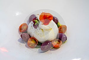 A caprese salad with mozzarella cheese made with donkey\'s milk, colored cherry tomatoes and basil, all on a white plate