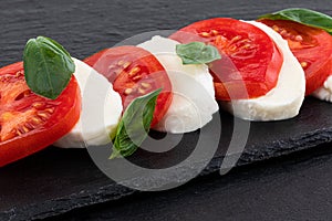 Caprese salad. Mozzarella cheese, tomatoes and basil herb leaves over stone table