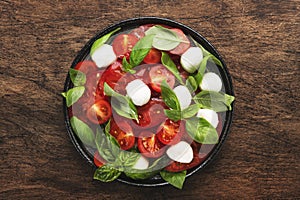 Caprese salad with ripe red tomatoes and mozzarella cheese with fresh green basil leaves. Italian food. Top view, wooden